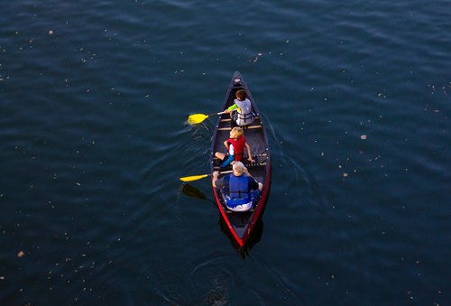 three people, a man and two boys, sit in a canoe in a lake of deep blue water