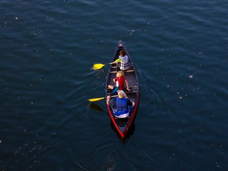 three people, a man and two boys, sit in a canoe in a lake of deep blue water