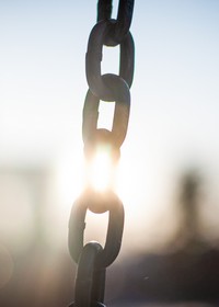 a metal chain with the sun shining through one of the links to make it look as if it is being severed from the rest