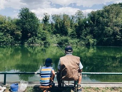 Older man and young boy sitting before a lake as they hold fishing poles and gaze at the water
