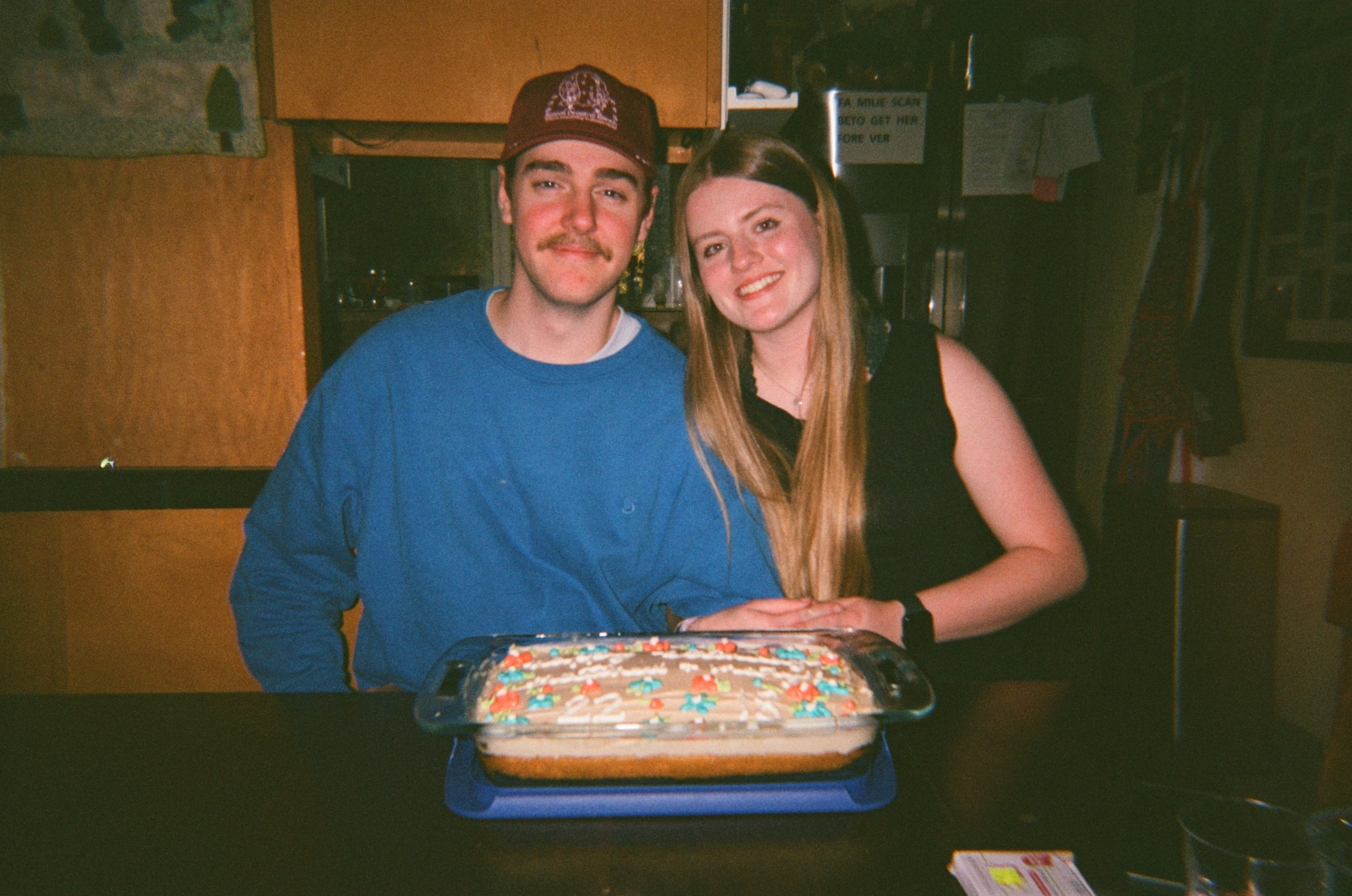 Photo of a young couple smiling with a birthday cake on the table in front of them.