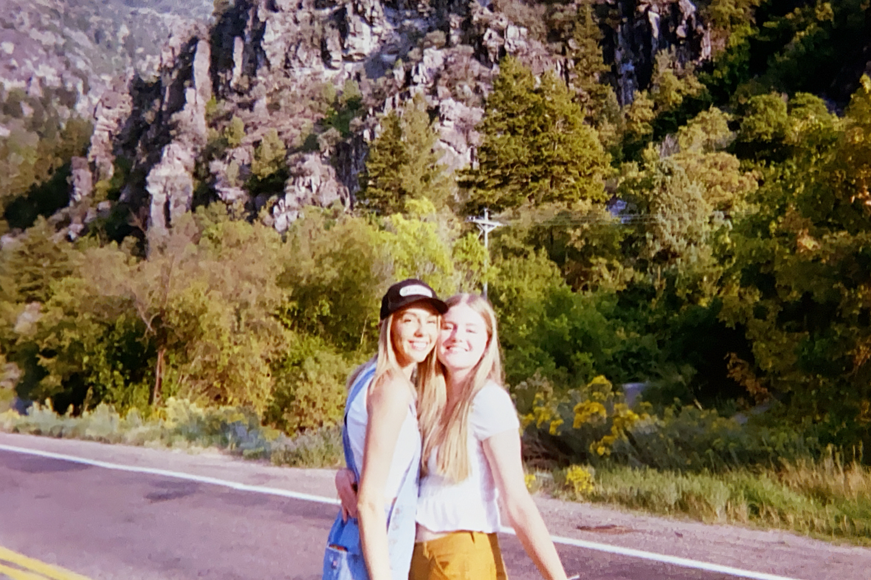 A young woman holding her diploma at high school graduation with one of her sisters on either side of her.