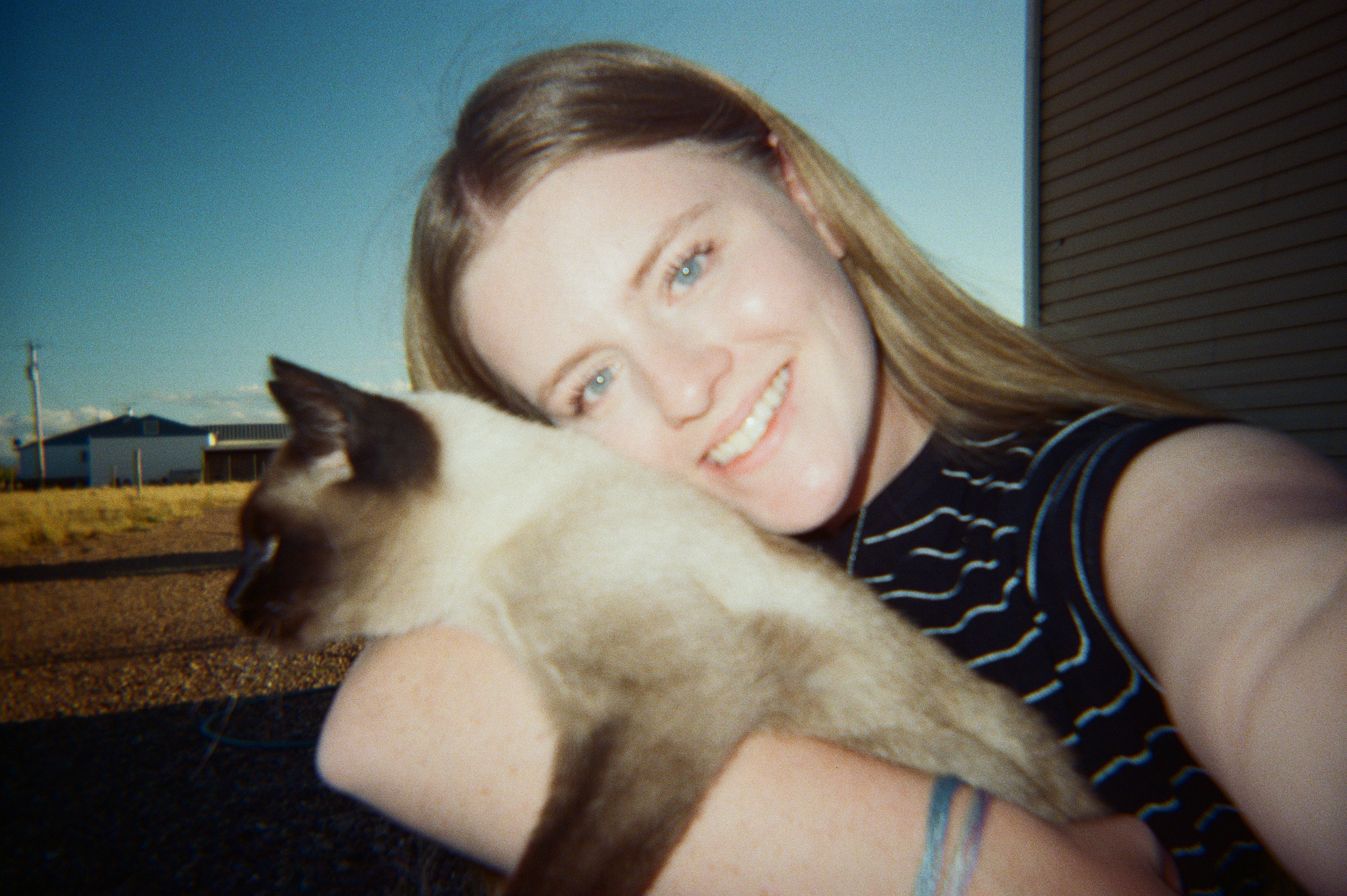 Selfie of a young woman holding a cat with her head pressed against it.