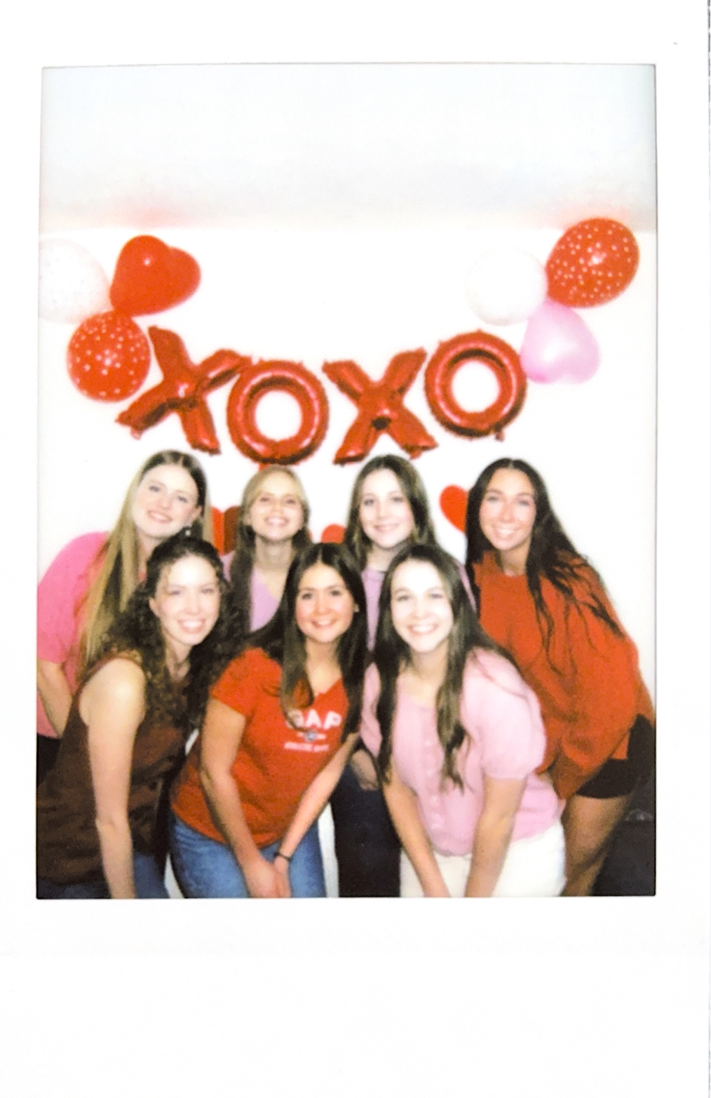 Seven young women in red and pink in front of a Valentine's display.
