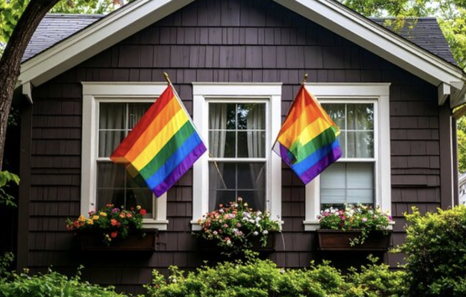 A brown home with two pride flags hanging in front of the windows.