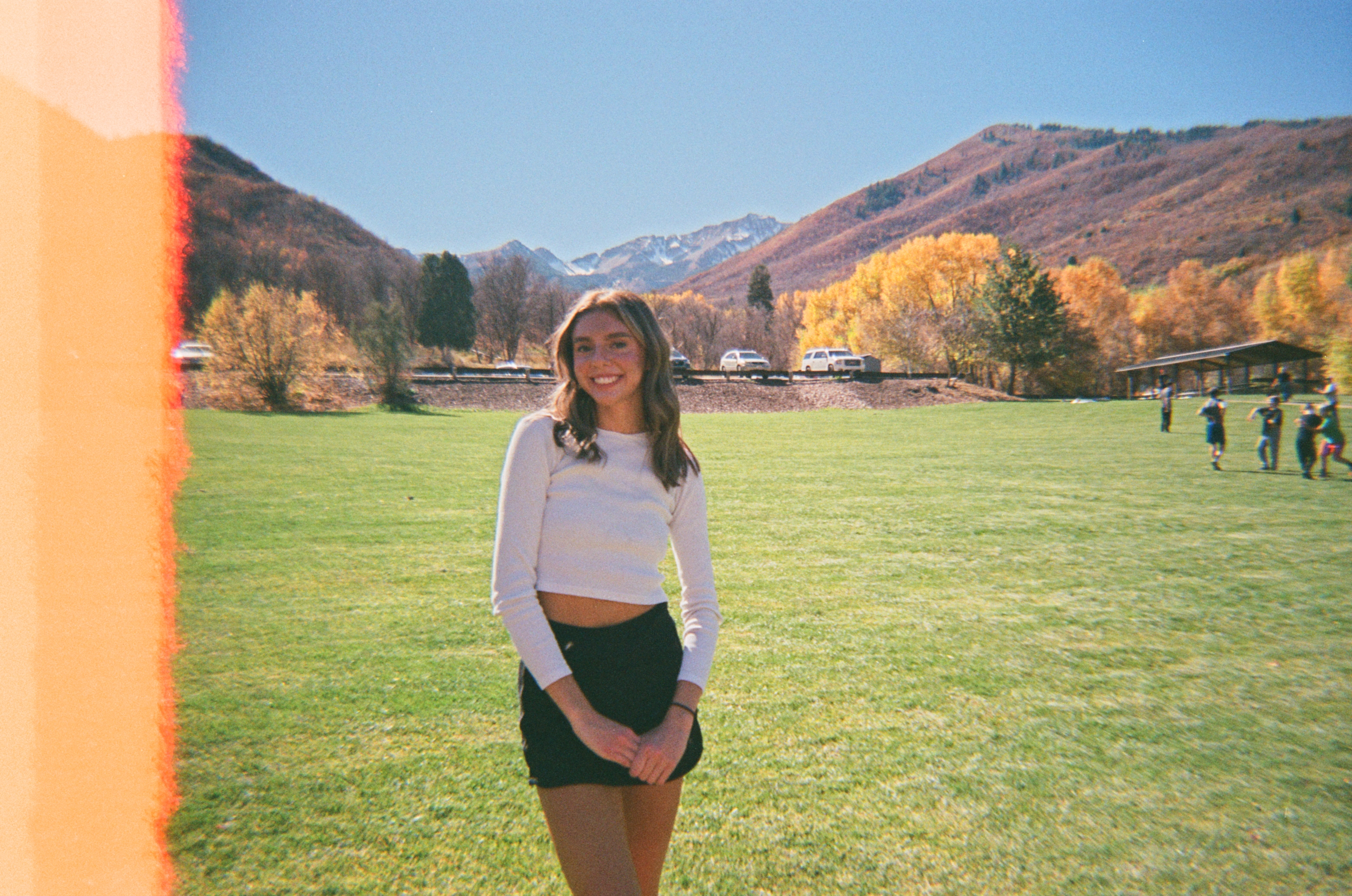 A young woman standing in a park in utah, orange light leak on the left side.