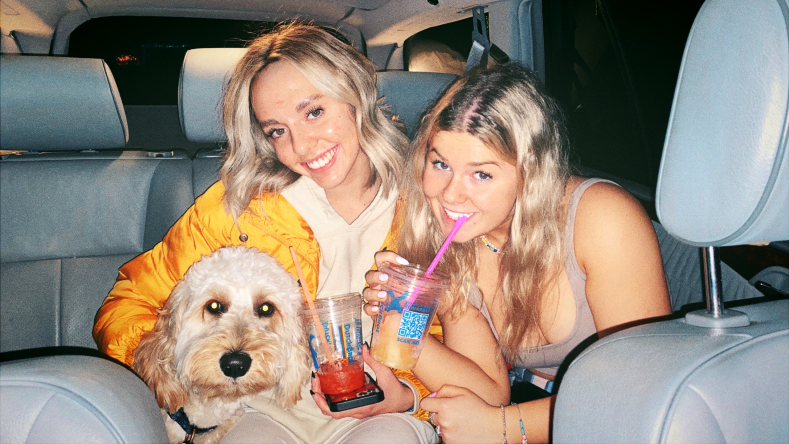 A young woman holding her diploma at high school graduation with one of her sisters on either side of her.