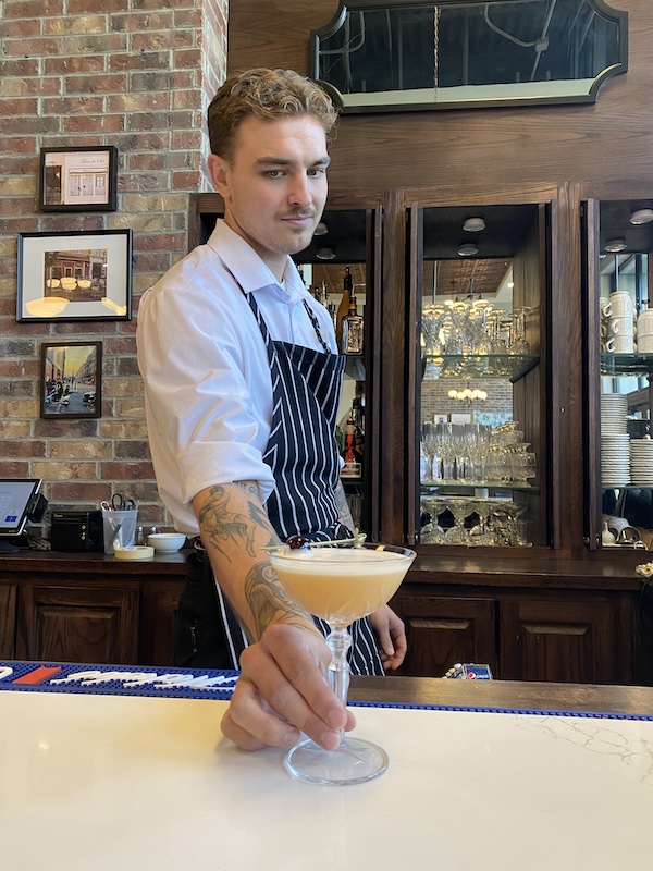 photo of Drew Wixom in bartending uniform, serving a cocktail