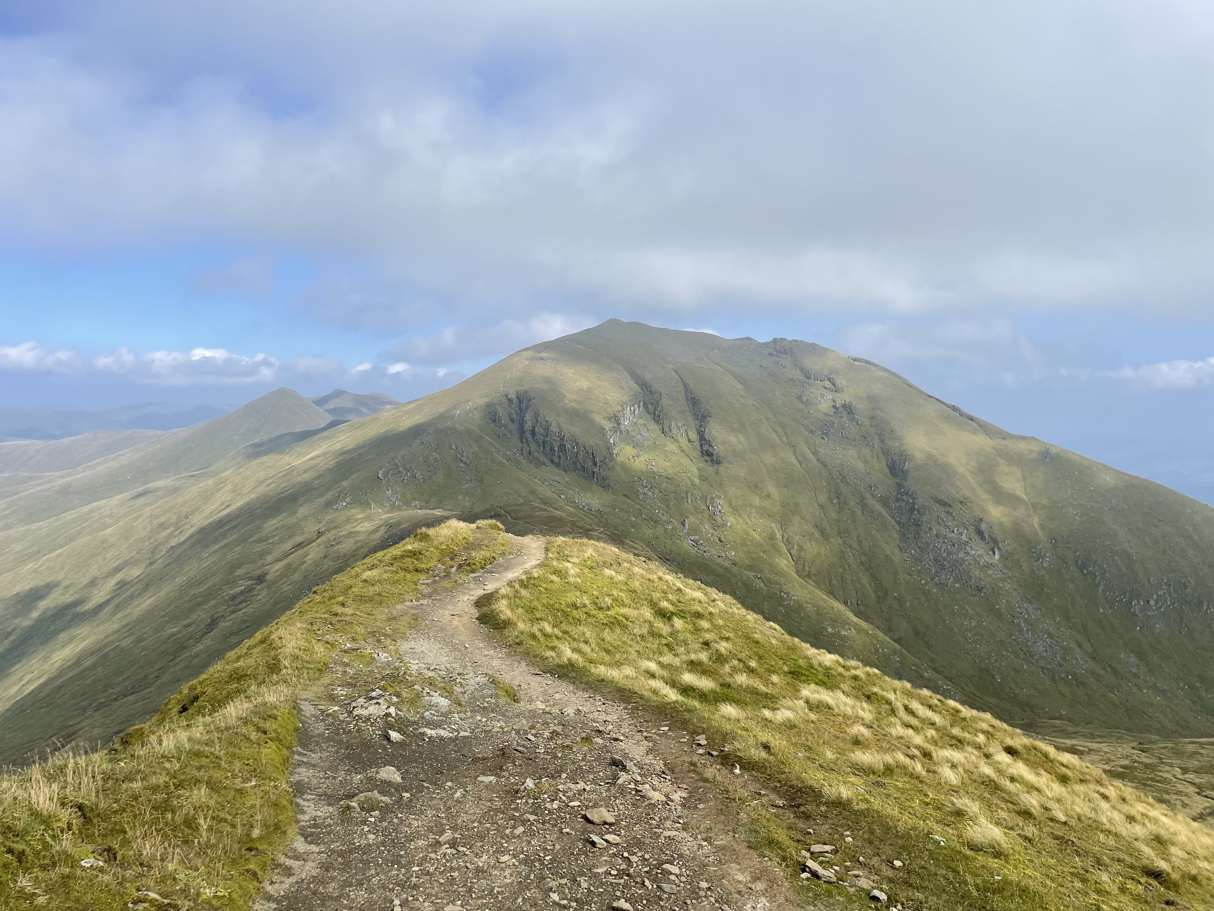 a rocky mountain pass with yellow-green grass on either side and low, gray clouds