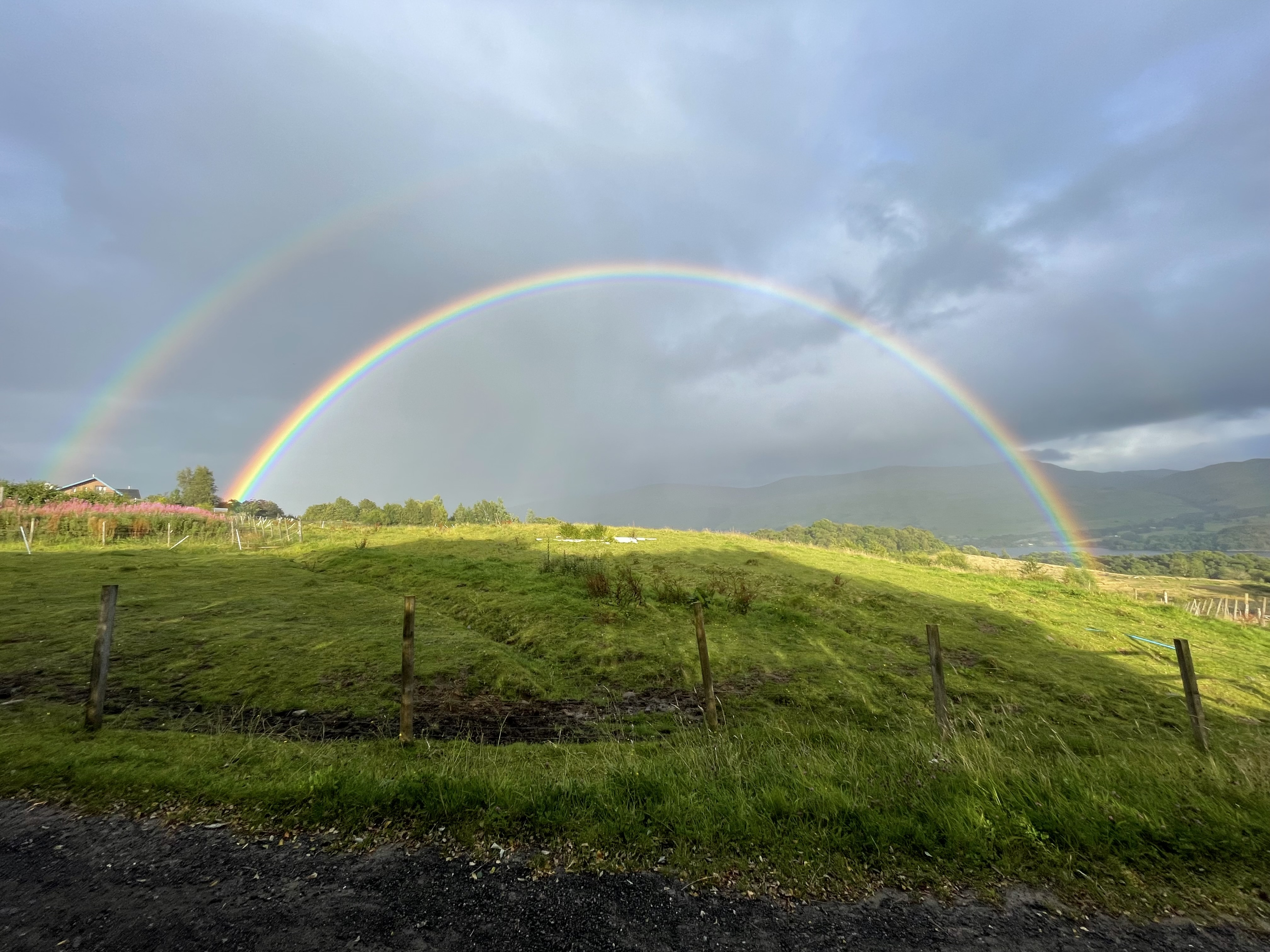 a vivid double rainbow over the green grass of the horse pasture