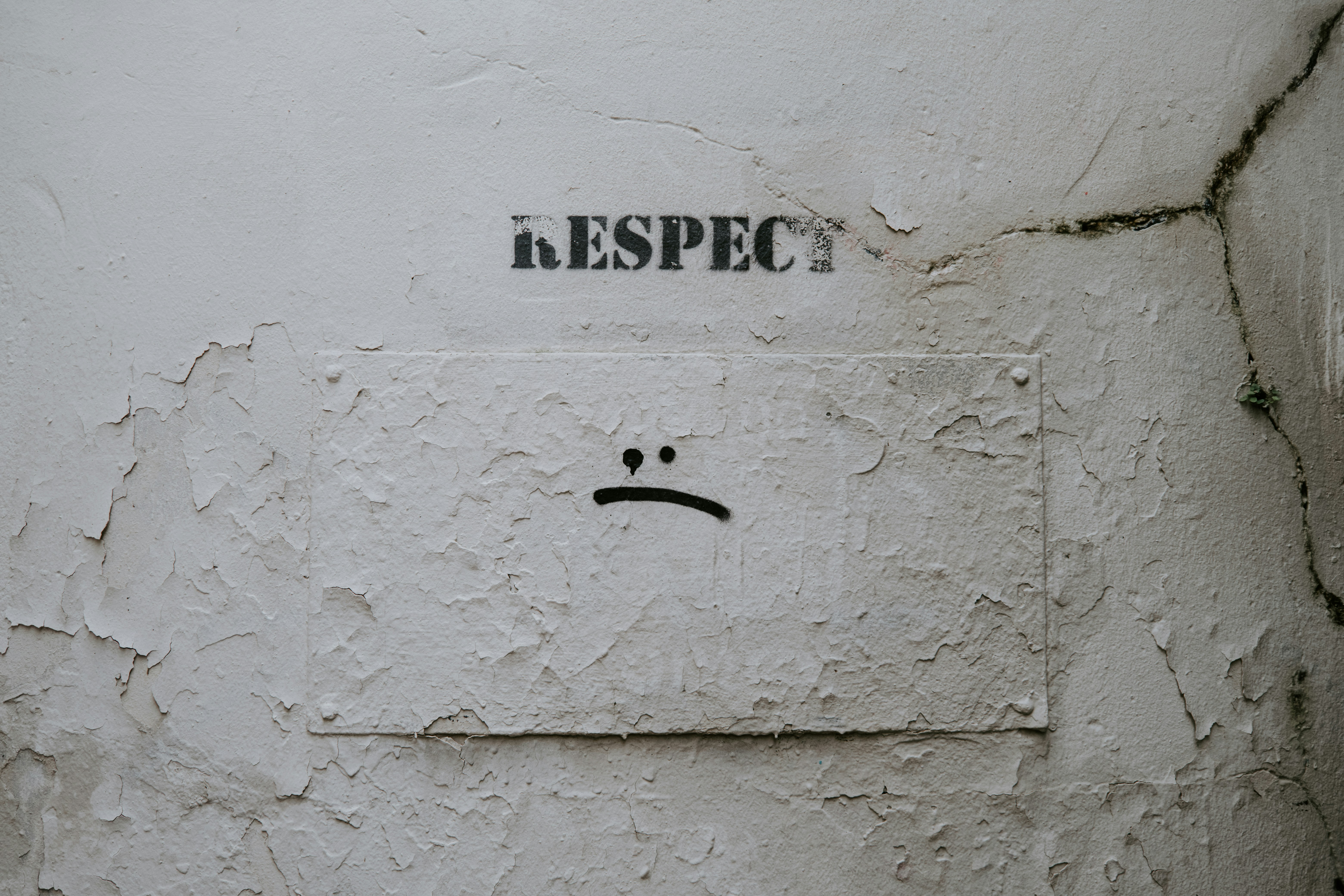 a white wall with the word 'respect' written in black block letters with a spray-painted frowny face below