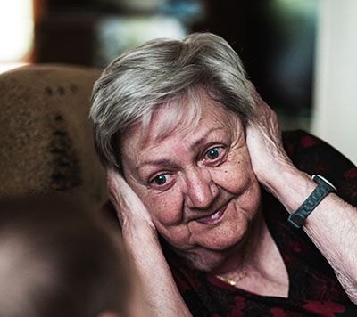 Older woman with her hands over her ears to avoid listening to a conversation.