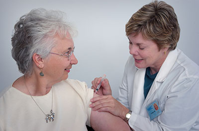 Baby Boomer-aged woman receives a vaccine from a woman roughly a generation younger.