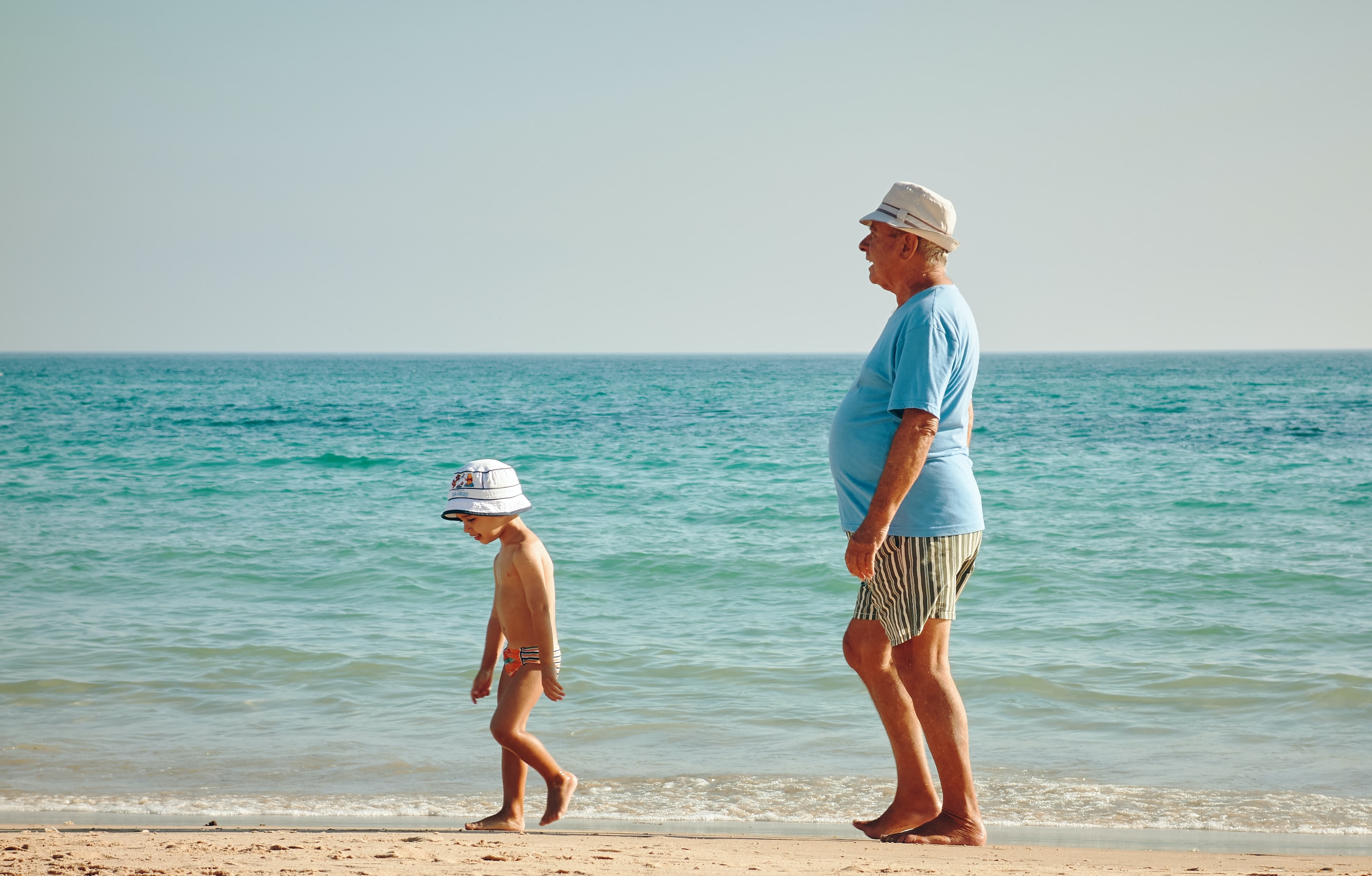 Old man and young boy walk together on the shore of a beach.